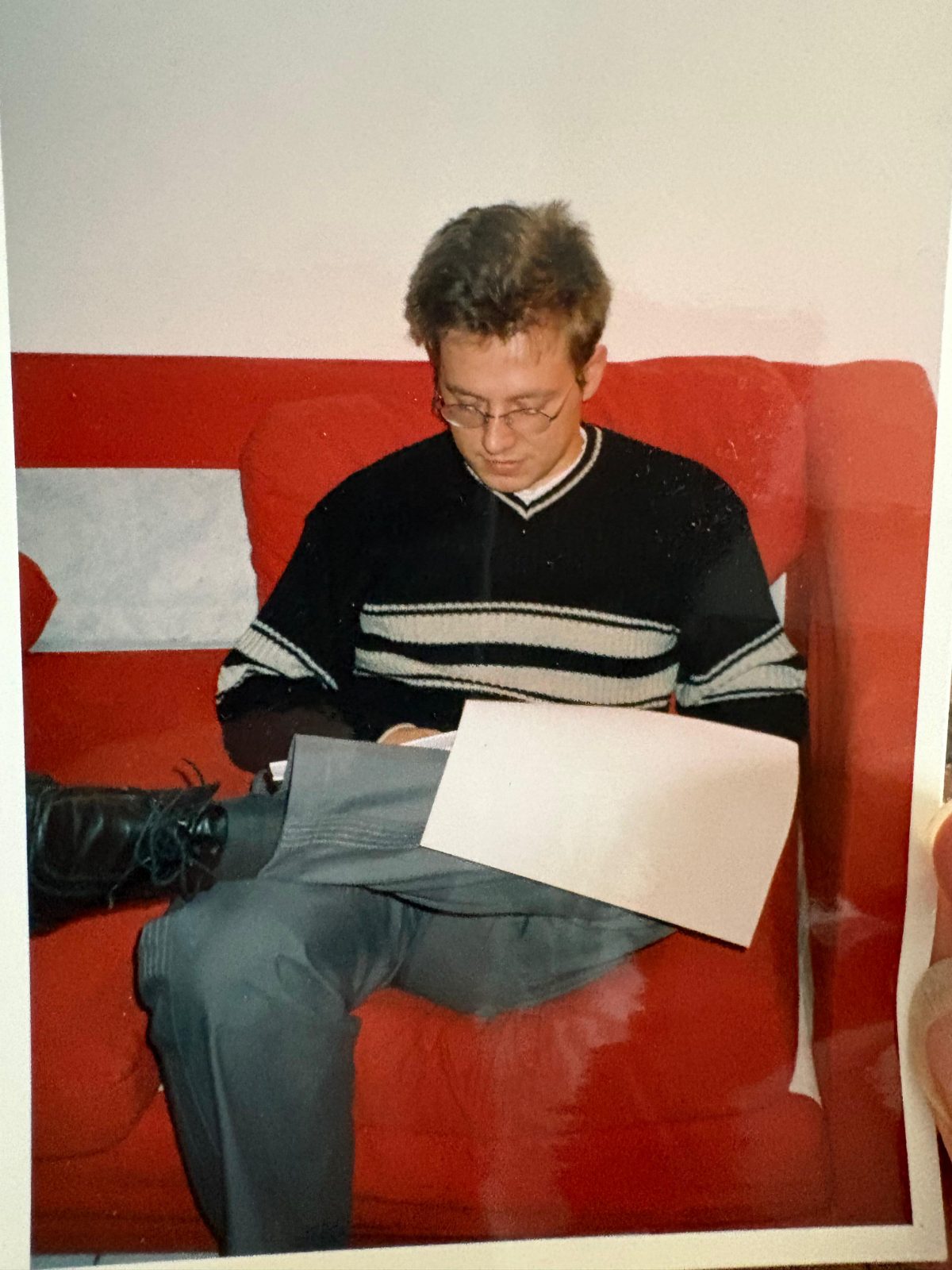 A print from the thesis years: Nicolas Boitout, in glasses and a striped jumper, sitting on a red sofa and reading a sheet of paper on his lap.